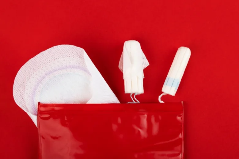 Červená taška s menstruačními vložkami a tampóny na červeném pozadí.
