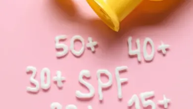 Žlutá lahvička s opalovacím krémem vytváří text SPF na růžovém pozadí