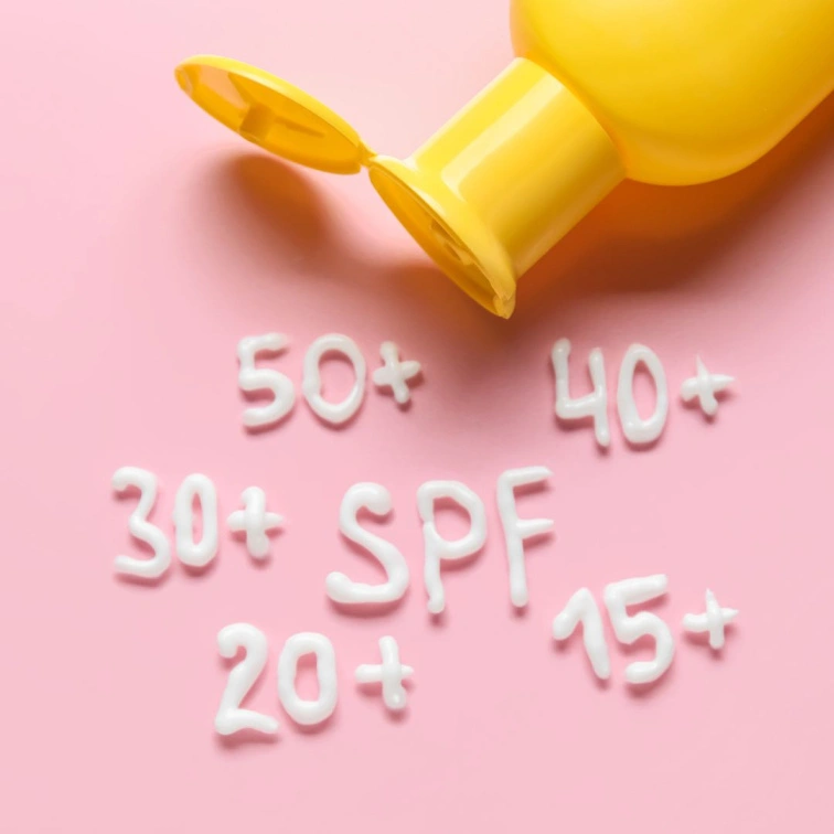 Žlutá lahvička s opalovacím krémem vytváří text SPF na růžovém pozadí