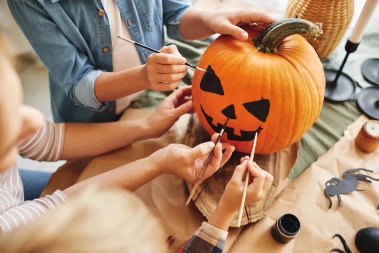 Lidé malují černé detaily na dýni pro halloween.