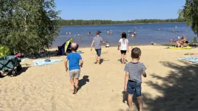 Děti hrají na pláži u jezera s dalšími lidmi ve vodě.