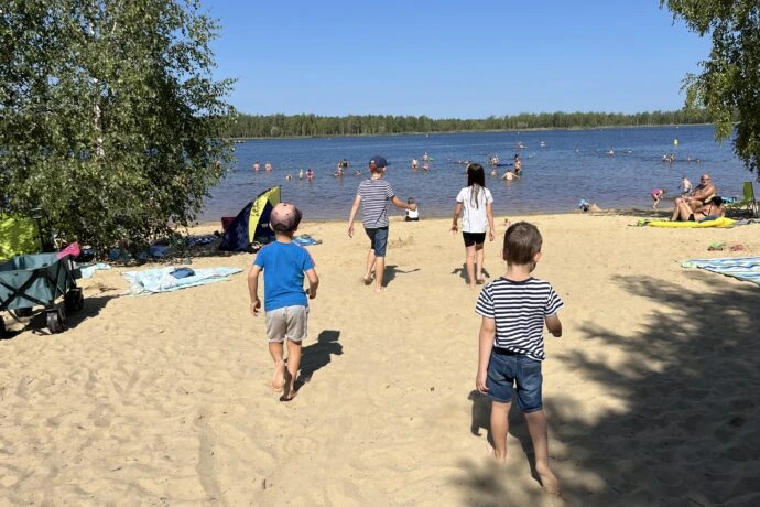 Děti hrají na pláži u jezera s dalšími lidmi ve vodě.
