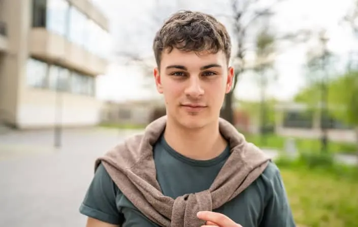 Mladý muž stojí venku s klidným výrazem ve svém oblečení.