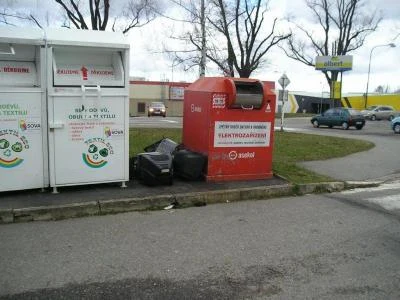 Bílé kontejnery na recyklaci vedle červeného kontejneru pro elektřiny odpady.