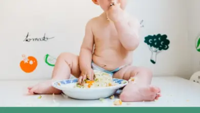 Malé dítě sedí na zemi a jí rýži s mrkví rukama.