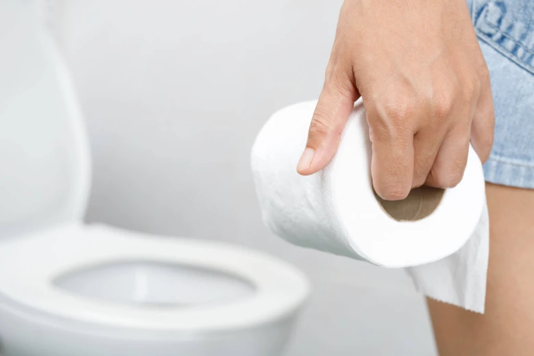 Ruka drží toaletní papír před otevřeným záchodem