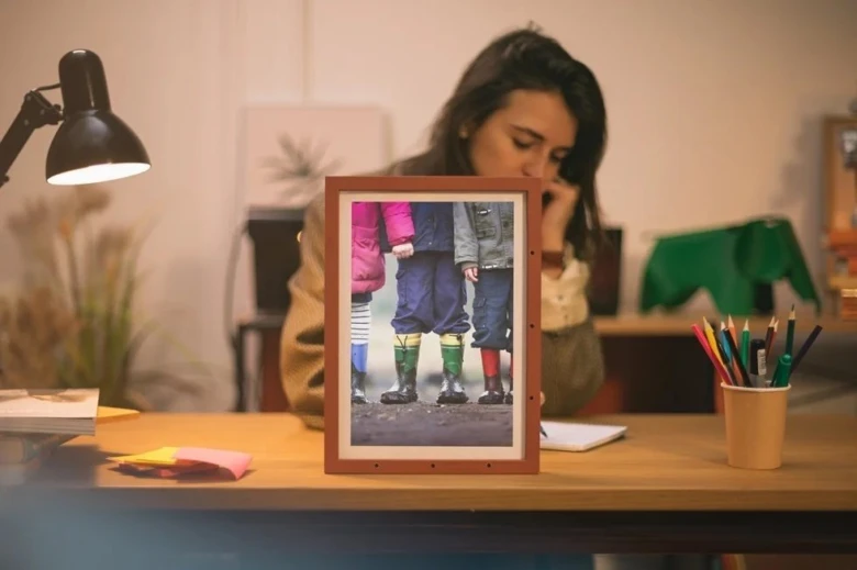 Žena sedí u stolu s rámečkem fotografií tří dětí.