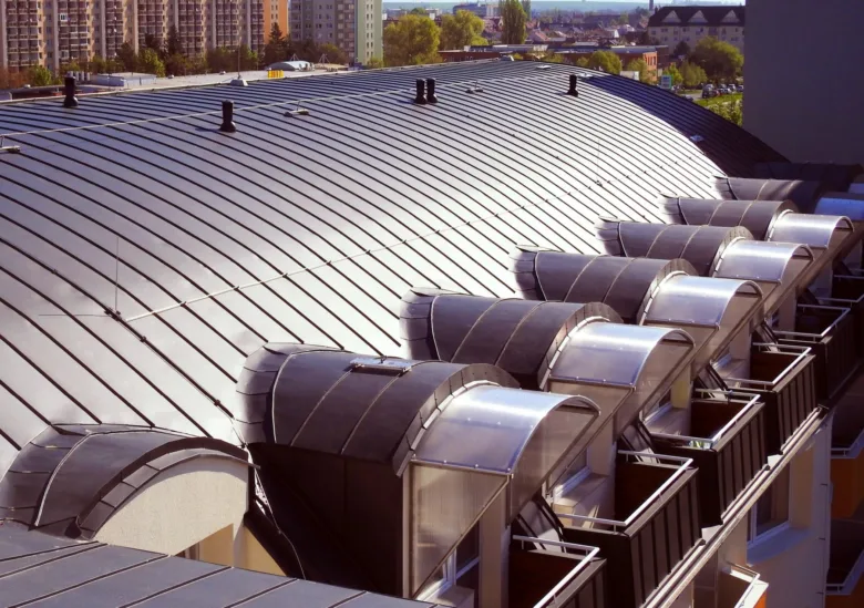 Falcovaná střecha s ventilátory na pozadí města.