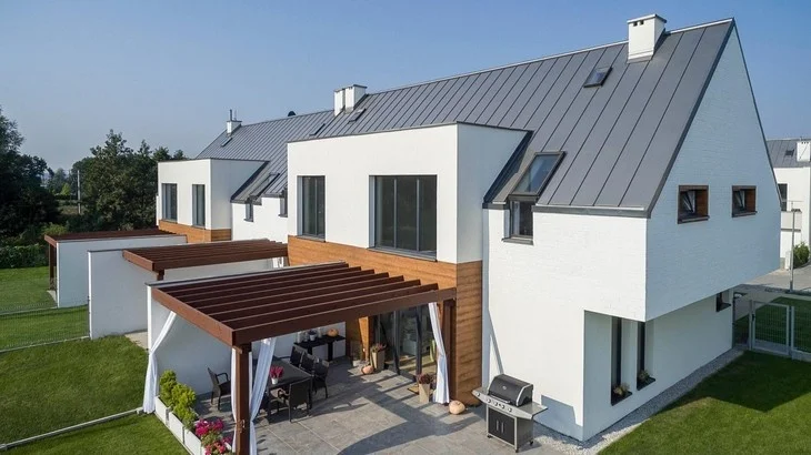 Moderní dům s tmavou falcovanou střechou a dřevěnou terasovou konstrukcí.