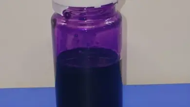 Fialová tekutina ve skleněné lahvičce na modrém povrchu.