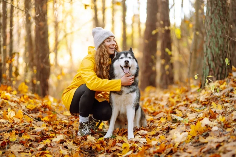 Žena v žluté bundě sedí s husky na podzimní stezce.