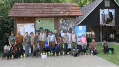 Skupina lidí s psy na venkově u budovy.