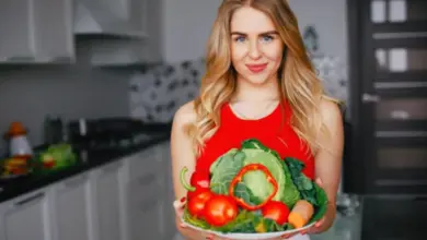 Žena drží talíř čerstvé zeleniny v kuchyni.