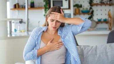 Žena sedí na gauči s rukou u čela jako by měla bolesti hlavy.
