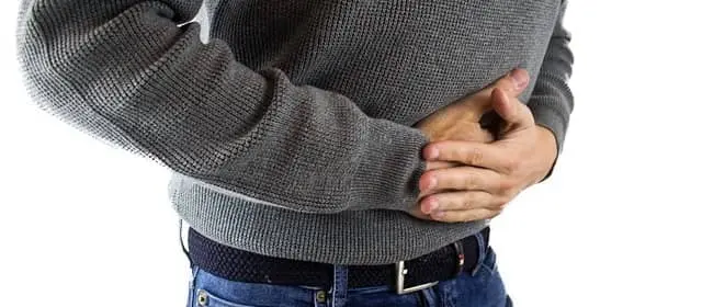 Muž drží žaludek v bolesti při trávicích potížích.