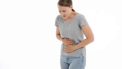 Žena drží břicho v bolesti na bílém pozadí.