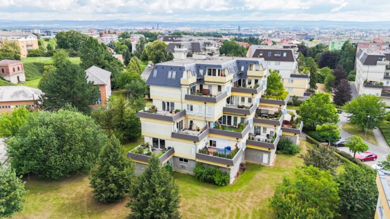 Moderní činžovní dům s balkóny uprostřed zeleně v českém městě.