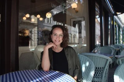 Usmívající žena sedí sama u venkovní kavárny.