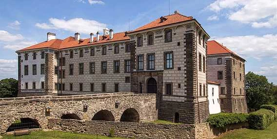 Zámek Veltrusy s červenou střechou na modrém nebi.