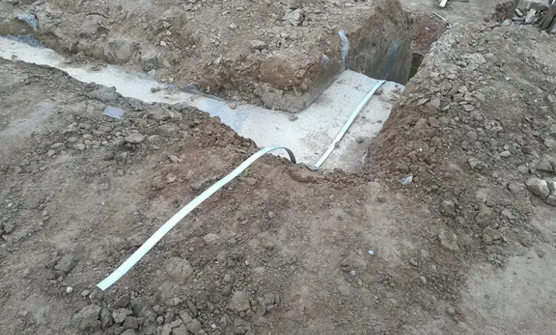 Bílý hromosvod je ukládán do výkopu vedle betonového základu při instalaci uzemnění.