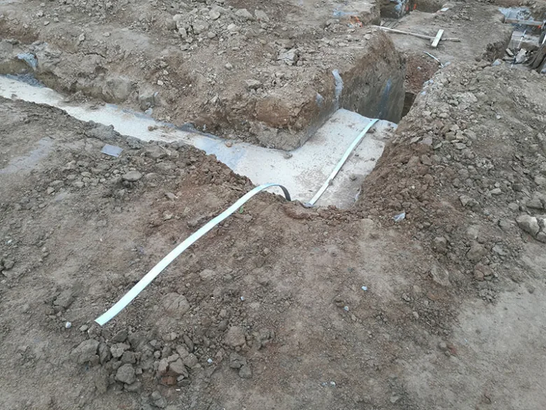 Bílý hromosvod je ukládán do výkopu vedle betonového základu při instalaci uzemnění.