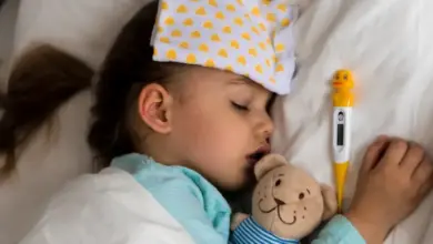 Spící nemocná dívka s teploměrem v posteli.