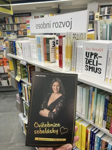Ruka drží knihu o sebepřijetí v knihkupectví na polici osobního rozvoje.