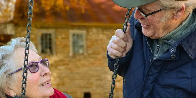 Starší pár se směje na houpačce před zdí.