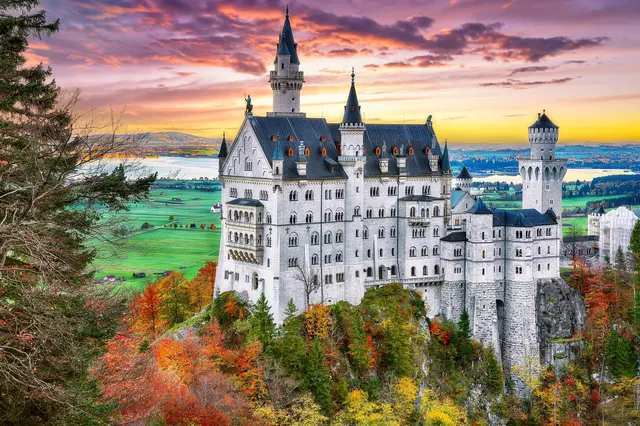 Bílý hrad Neuschwanstein na kopci s podzimními stromy.