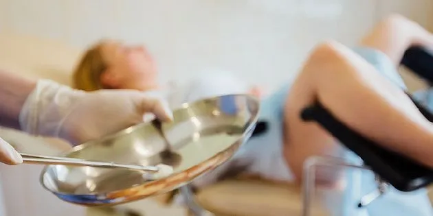 Lékař drží nástroje během gynekologického vyšetření pacientky.