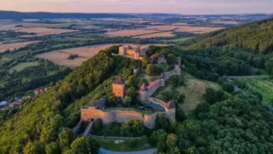 Pohled na středověký hrad s věžemi na kopci v krajině.