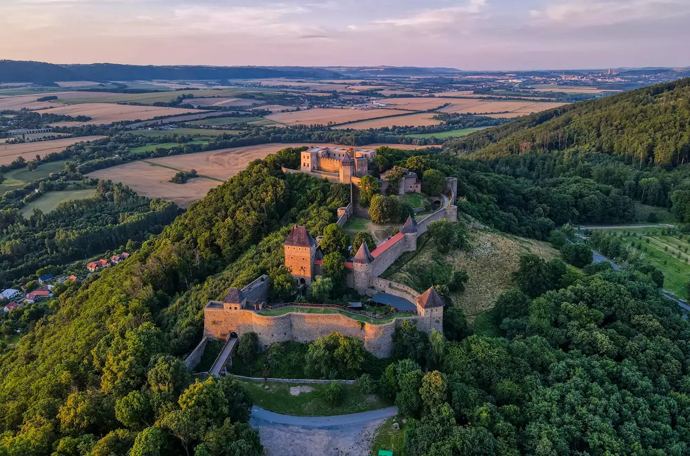 Pohled na středověký hrad s věžemi na kopci v krajině.