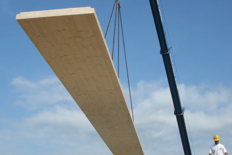 Velký dřevěný CLT panel je zvedán kranem na staveništi.