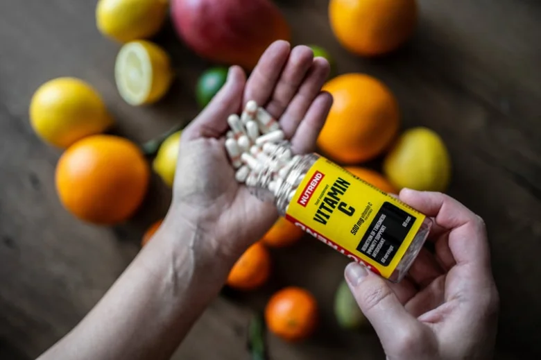 Ruce sypou bílé tablety vitamínu C mezi čerstvé citrusové plody.