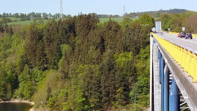 Žďákovský most přes lesnaté údolí s auty na silnici.