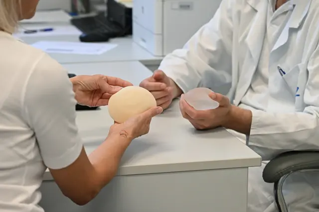 Lékař s pacientkou zkoumá různé typy implantátů pro rekonstrukci prsu.