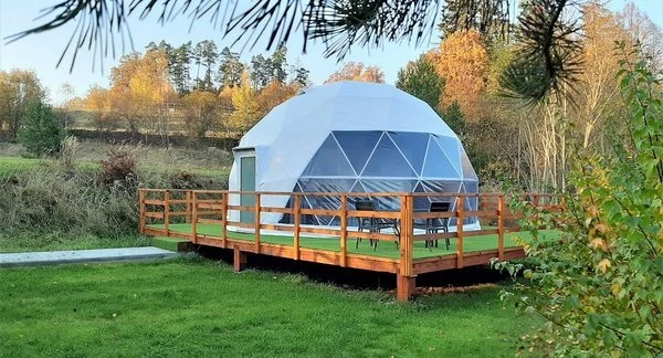 Bílá kupole pro glamping na dřevěné terase v přírodě.