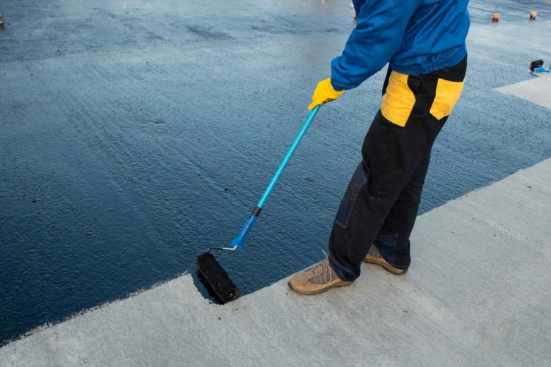 Pracovník nanáší tmavě modrý polymer na betonovou plochu válečkem.