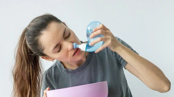 Žena používá k nosnímu zavlažování modrou nádobu na nachlazení.