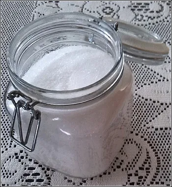 Sklenice s bílým práškem na krajkovém ubrousku.