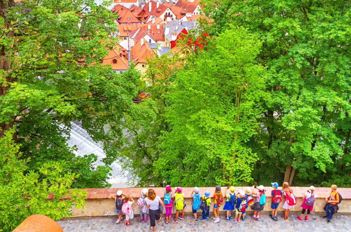 Skupina dětí s batohy hledí na české město z výhledu.