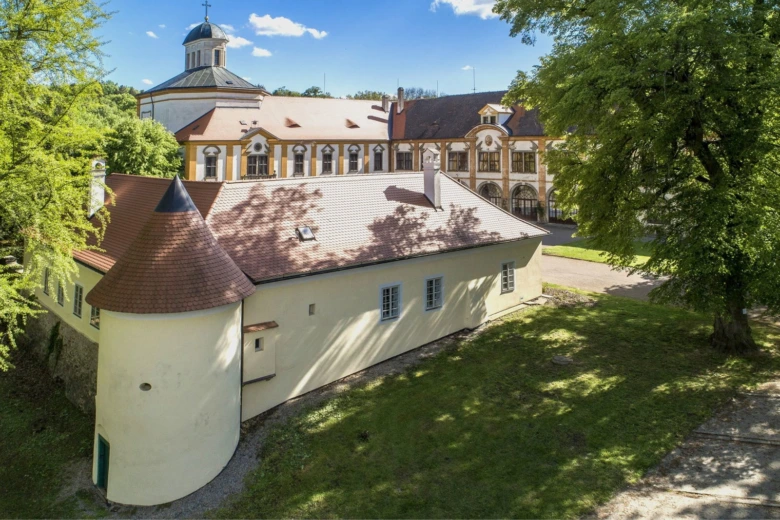Historické zámek s věží v zeleném parku.