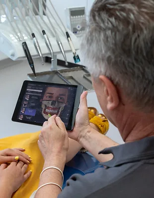 Zubní lékař s pacientem zkoumá digitální sken zubů na tabletu pro plánování ošetření moudrosti.