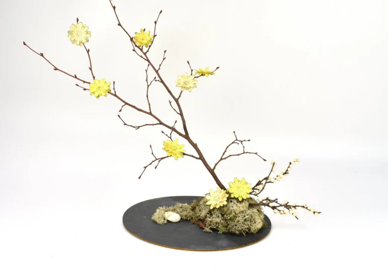 Hotový ikebana s žlutými květy na tmavém podstavci.