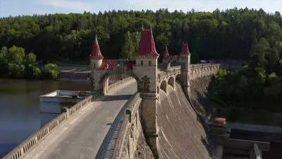 Žďákovský most přes řeku s červenými střechami v přírodě.