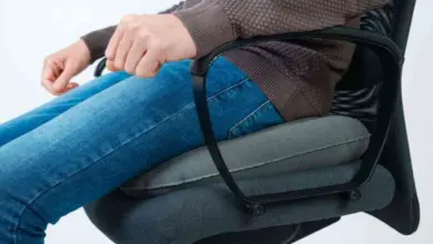 Osoba sedí na židli s polštářem pro dolní část zad.