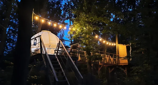Bílá kupole pro glamping mezi stromy s osvětlením v Brdech.