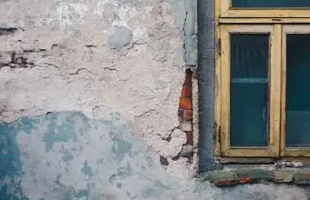 Zvětralá omítka na zdi u okna symbolizující depersonalizaci.