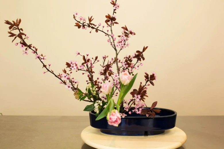 Japonská Ikebana s růžovými květy v černé mise na světlém podstavci.