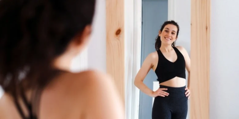 Žena se usmívá do zrcadla v sportovní oblečení.